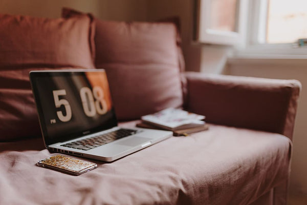 laptop, celular de capa dourada e cadernos sobre sofá de capa rosa