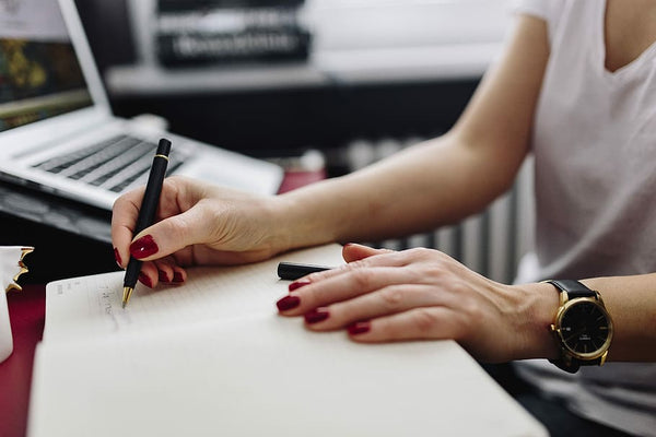 mulher faz anotações no caderno com laptop ao lado em ambiente de trabalho