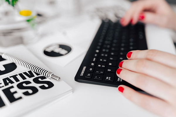 mulher de unhas vermelhas digitando no teclado com cartões ao redor e caneta