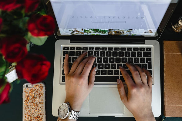 mulher trabalhando no laptop com arranjo de rosas vermelhas ao lado e celular com capinha personalizada ao lado