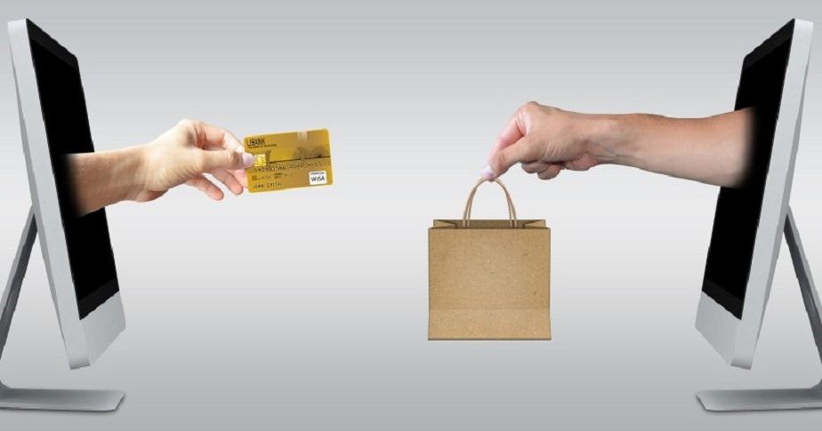 mão entrega sacola pela tela do computador para outra mão segurando um cartão de crédito, ilustrando artigo sobre exemplos de e-commerce