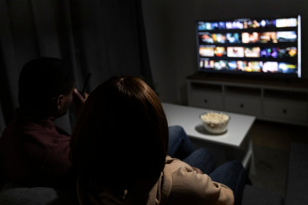 Casal no sofá de casa com pipoca a postos escolhendo o que assistir em plataforma de streaming