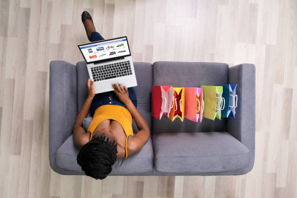 mulher faz compras no laptop ao lado de sacolas de compras coloridas no sofá