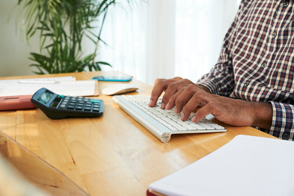 homem digitando no teclado do computador em sua mesa de trabalho com calculadora em frente