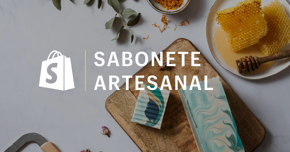 Fotografia que mostra, em um fundo branco, todos os ingredientes envolvidos no processo de fabricação de um sabonete artesanal. O sabonete está em uma tábua de madeira, mais ou menos centralizado, e é azul e branco. No primeiro plano, ao lado do logo da Shopify, está escrito "sabonete artesanal"