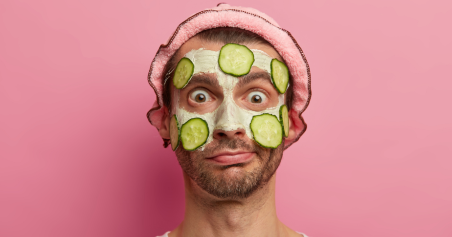 Massageadores faciais com LED e outros produtos de skincare estão entre o que mais vende hoje na internet. A foto mostra, com um plano de fundo rosa, um homem com creme e pepinos na cara, como se estivesse fazendo uma rotina de skincare.
