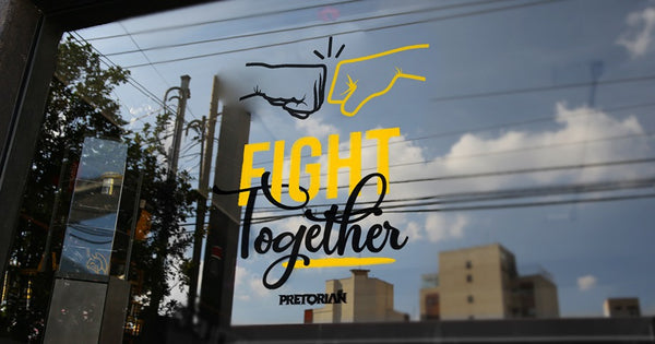 Foto mostra uma vitrine escura, com os dizeres "Fight together, Pretorian". Na vitrine, não é possível ver o interior, apenas o reflexo do céu e de prédios.