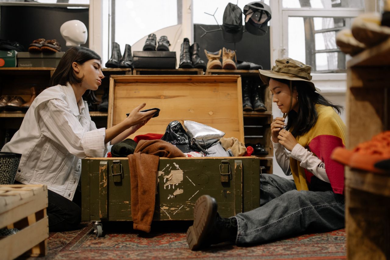 Duas mulheres sentadas no chão selecionando roupas em um baú