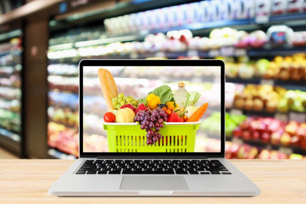 cesta com produtos de supermercado na tela do laptop e mercado desfocado ao fundo