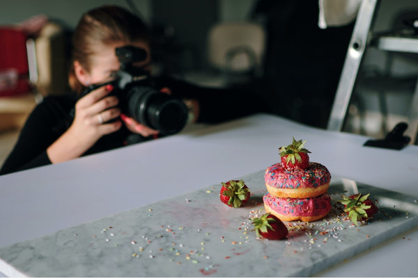 Mulher fotografa donuts em cima de uma mesa cinza, representando a fotografia, um exemplo de como empreender com pouco dinheiro