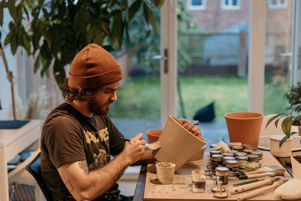 Homem pinta vaso de cerâmica, representando a venda de produtos artesanais, um exemplo de como empreender com pouco dinheiro