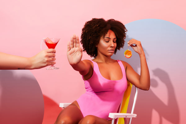Foto de artigo sobre mulheres empreendedoras mostra uma mulher sentada em uma cadeira de praia, segurando um disco menstrual com a mão esquerda. Com a mão direita estendida, ela recusa uma taça com um líquido vermelho e um absorvente interno dentro.