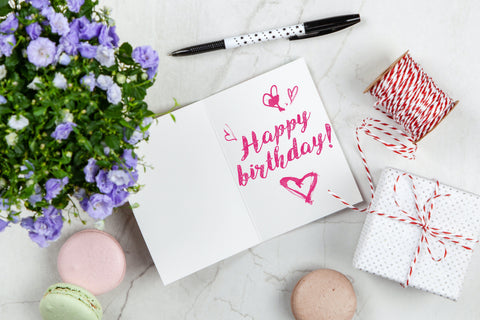 Flores, cartão com "happy birthday!" escrito a mão, macarons, caixinha de presente e barbante