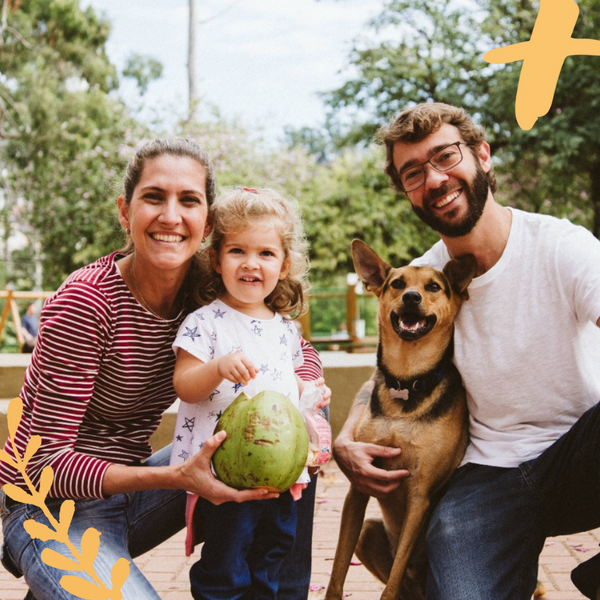 Foto da família da fundadora da Mama+ mostra Marina, uma mulher, abraçada com uma criança de aproximadamente 4 anos, ao lado de um homem que abraça um cachorro.