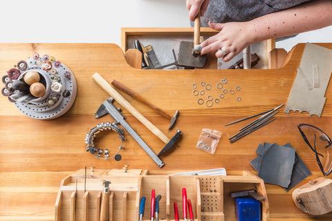 Mesa com ferramentas e materiais, mãos de uma pessoa confeccionando bijuterias
