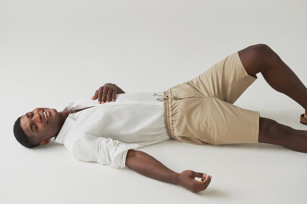 Foto de artigo sobre moda atemporal mostra uma pessoa deitada em um chão branco, usando uma camisa social branca e um short bege.