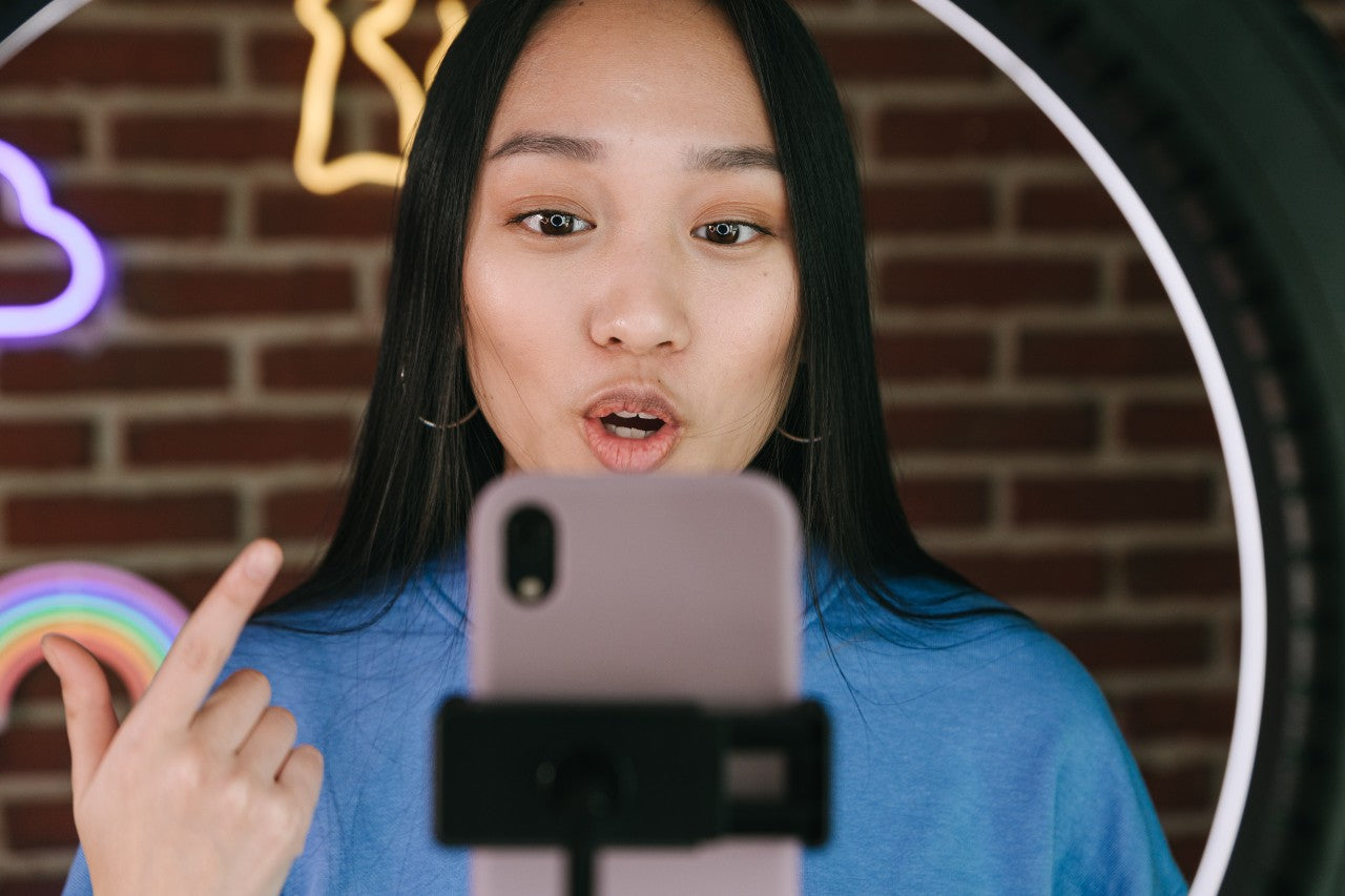 Jovem de origem asiática grava um vídeo em seu celular, falando diretamente para a câmera