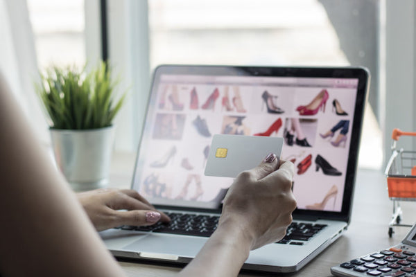 mulher olhando catálogo online de sapatos no laptop com cartão de crédito na mão
