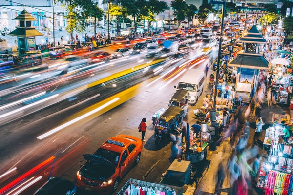 Foto do artigo sobre tráfego pago mostra uma avenida movimentada, onde é possível ver carros em alta velocidade e, à direita da imagem, uma calçada cheia de pedestres e barracas de vendas.