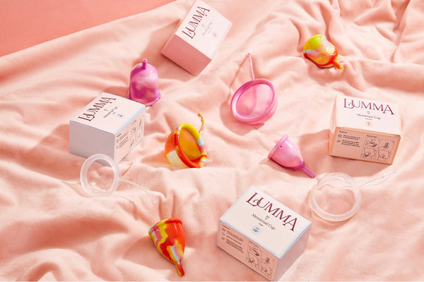 Foto sobre empreendedorismo feminino mostra diversos copos e discos menstruais sobre um cobertor. Há também embalagens dos produtos menstruais com o logo da Lumma.