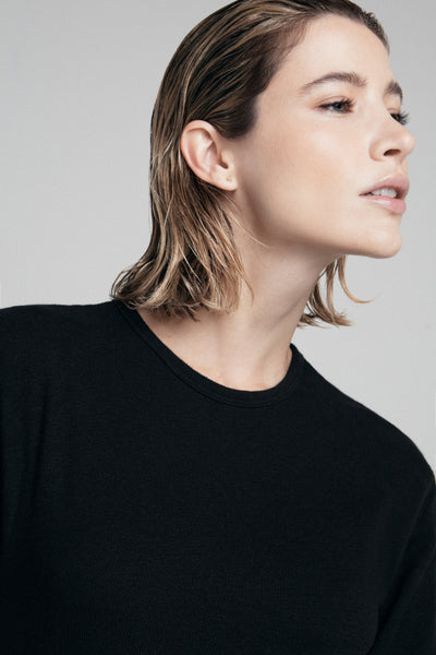 Foto de moda atemporal mostra uma pessoa de cabelos claros e curtos vestindo uma camiseta preta. A foto foca na parte superior do corpo da pessoa.