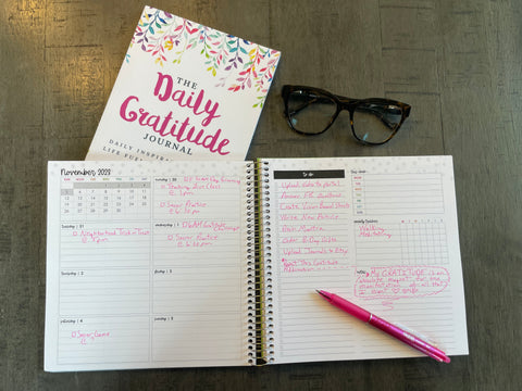 An 8x8" planner is open on a desk filled with plans and notes -- some of the pages contain gratitudes.