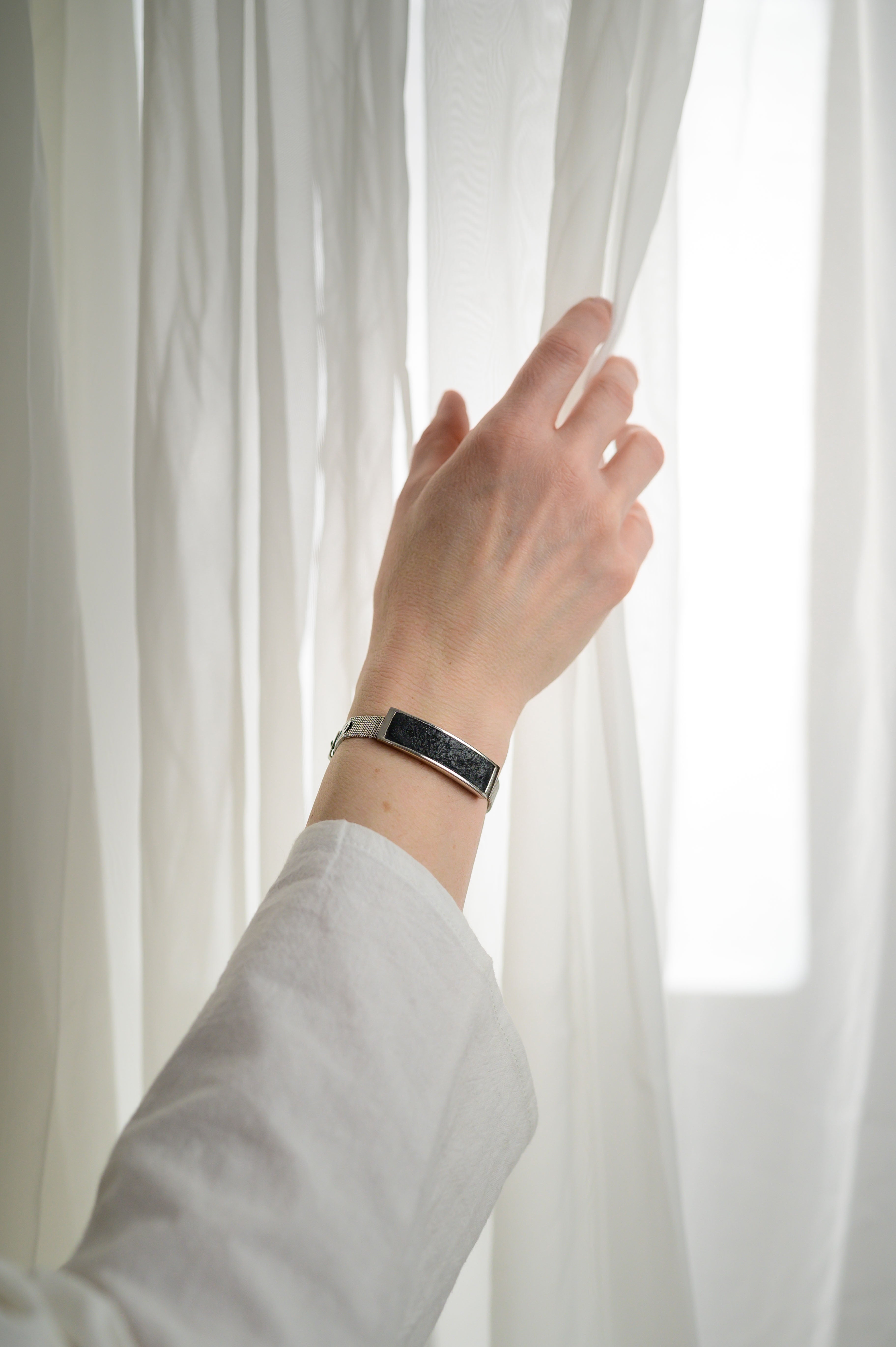 sheer curtain and hand with bracelet pulling it back