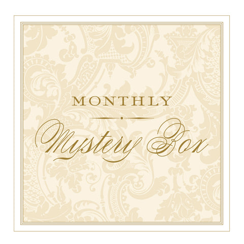 An ornate beige and gold label with the words "Monthly Mystery Box" in elegant script font, featuring exclusive Anna Griffin products.