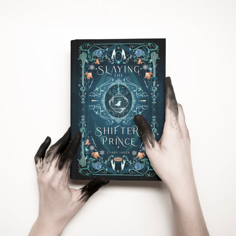 Slaying the Shifter Prince by Clare Sager under dust jacket artwork in teal featuring birds, collars, daggers, and women's hands – motifs that relate to this twisted beauty and the beast fantasy romance reimagining.