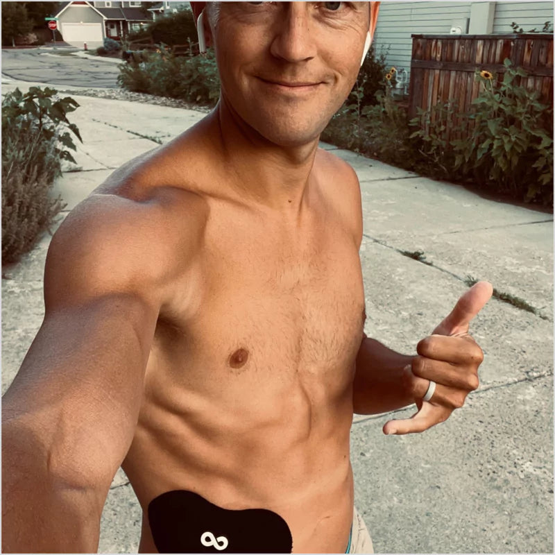 Man outdoors wearing a glucose monitor on his abdomen, posing for a selfie.