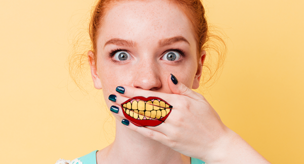 woman covering her mouth with her hands which has a mouth with a yellow teeth painted on it