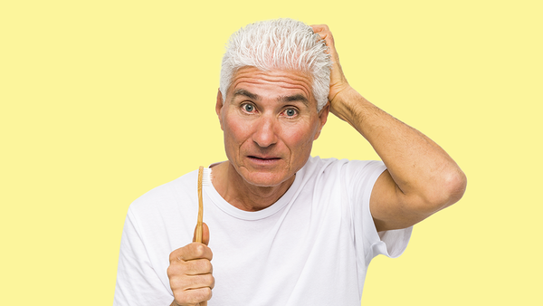 old man scratching his head holding a toothbrush