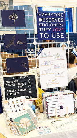 A snapshot of a craft fair stall where wire racking has been used to display art prints, with products on small stands at the front