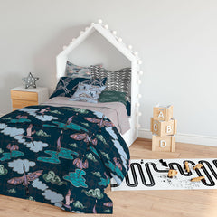 A single bed in a childs room, has a quilt cover of the Migrating Cranes pattern, along with a selection of pillows in complemetary pattterns. Alongside the bed is a bedside table, along with small wooden blocks and a childs play carpet on the wooden floor.
