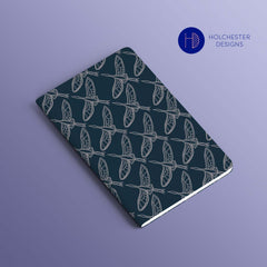 A Notebook, with teh Holchester Designs Flying Cranes print, is lying flat with Very Peri background behind it.