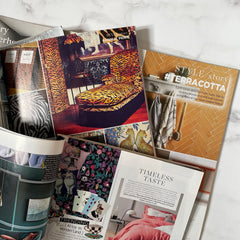 Three interiors magazines are open, piled on a marble tabletop.