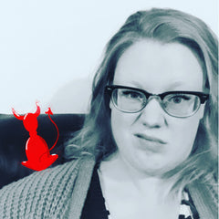 A black and white photograph of Rachel, a white woman in her 30s wearing glasses, sat on the sofa with a red devil illustration on her shoulder.