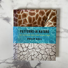 Patterns in Nature, a book by Philip Ball, is lying closed on a marble table top.