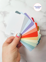 A hand holds out a fan of swatchos - credit card sized colour swatch cards - which are all warm pastel tones representing the summer palette.