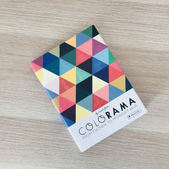 The book Colorama is lying flat on a wooden tabletop so you can see the multicoloured cover.