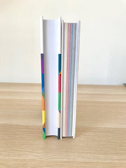 Two books stand upright on a wooden desk. The Page edges are faced towards you to see the colourful edges.