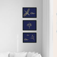 Three framed images hang on a white wall.  They all have dark navy backgrounds with gold foil Crane Motifs (either standing or flying). Infront of the wall is a white sofa, and white curtains hang on the window to the right.