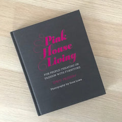 Pink House Living book - with a dark grey linen cover and hot pink foiled title - is lying on a wooden tabletop