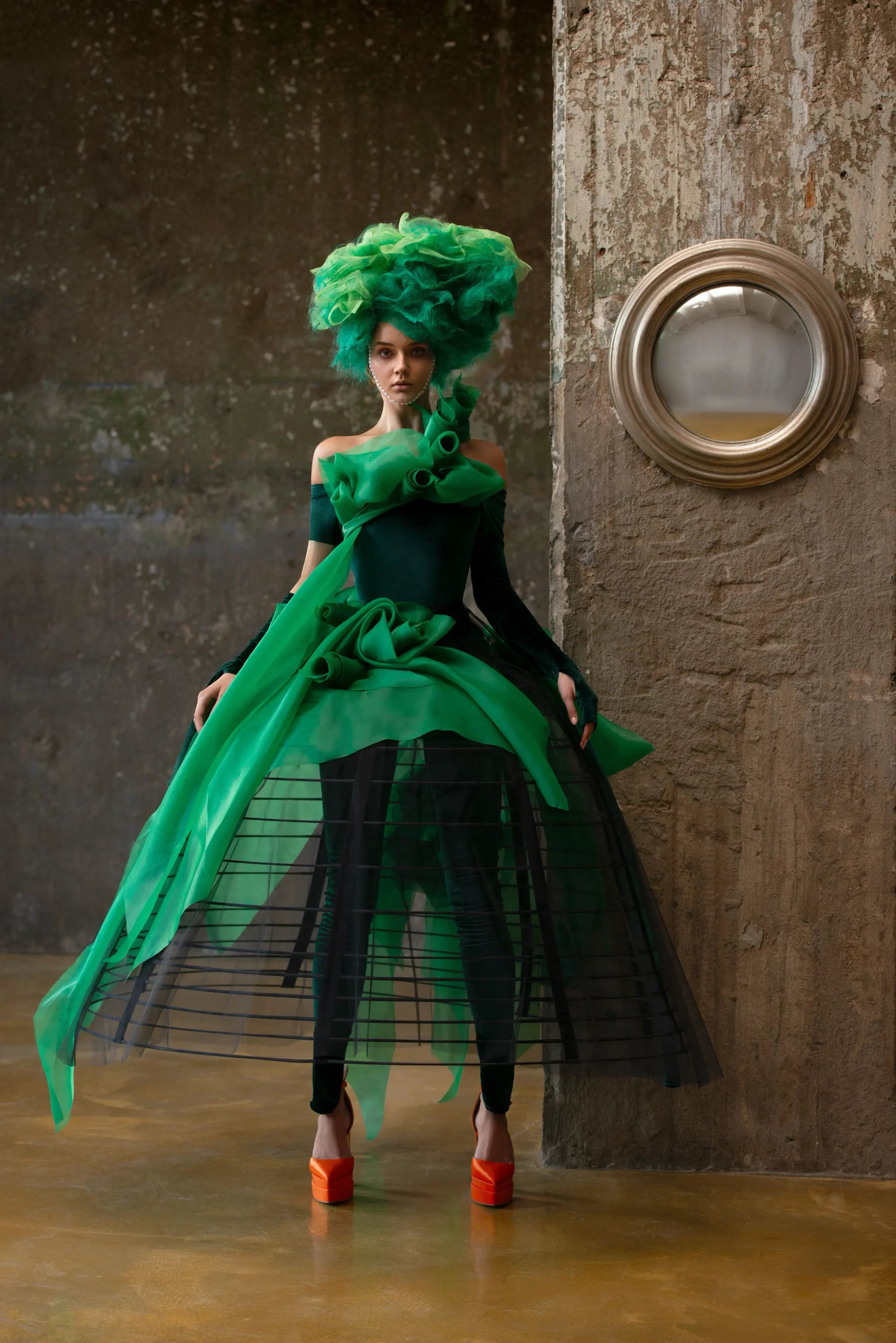 Model im grünen avantgardistischen Kleid mit transparentem Rock und großen orangefarbenen Plateauschuhen.