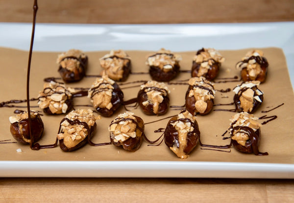 A baking sheet with chocolate being drizzled over peanut butter stuffed dates