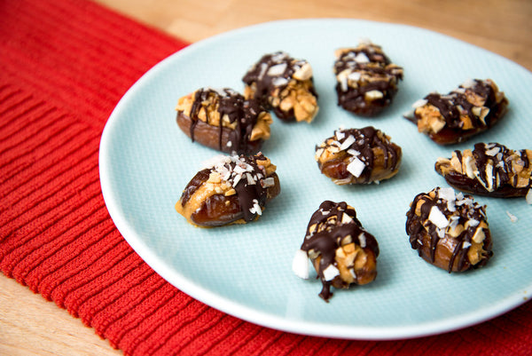 A plate of peanut butter stuffed dates with cashews and coconut and drizzled chocolate