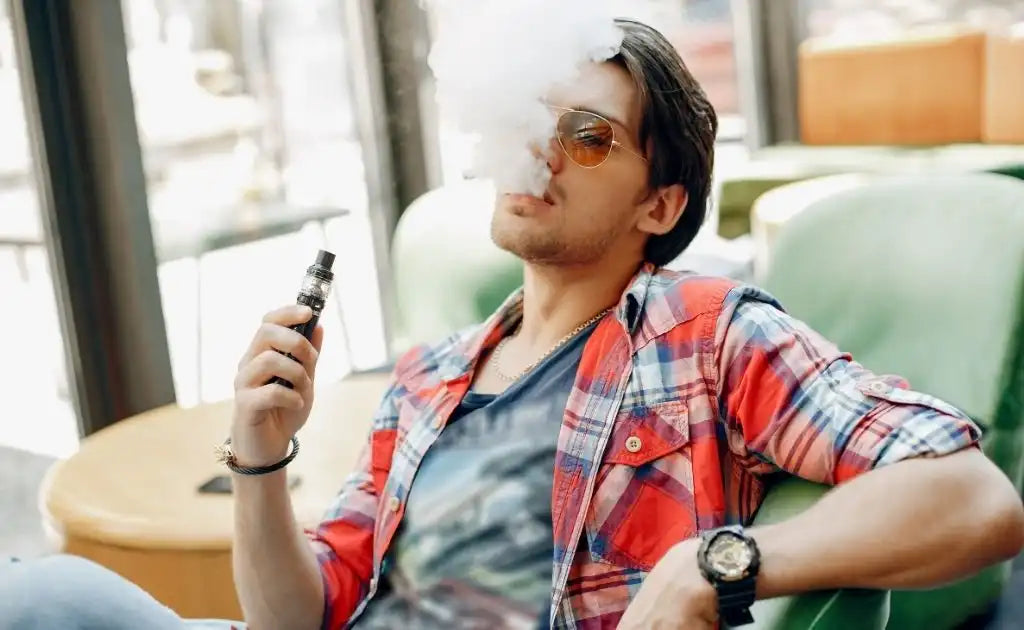 A man wearing sunglasses is casually smoking an electronic cigarette.