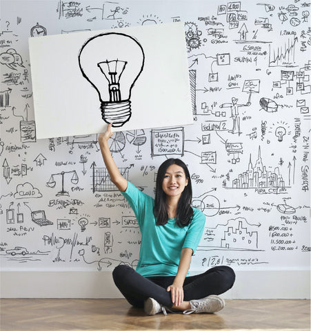 A woman set on the bedroom's land with showing a banner of lamp to show creative and inspiration to design home and decorate it, since the wall behind her is full of formula and text.