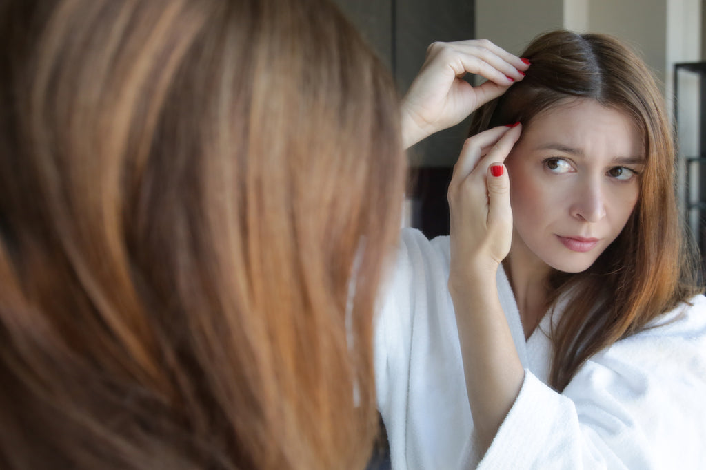 Young woman examining her scalp and hair in front of the mirror