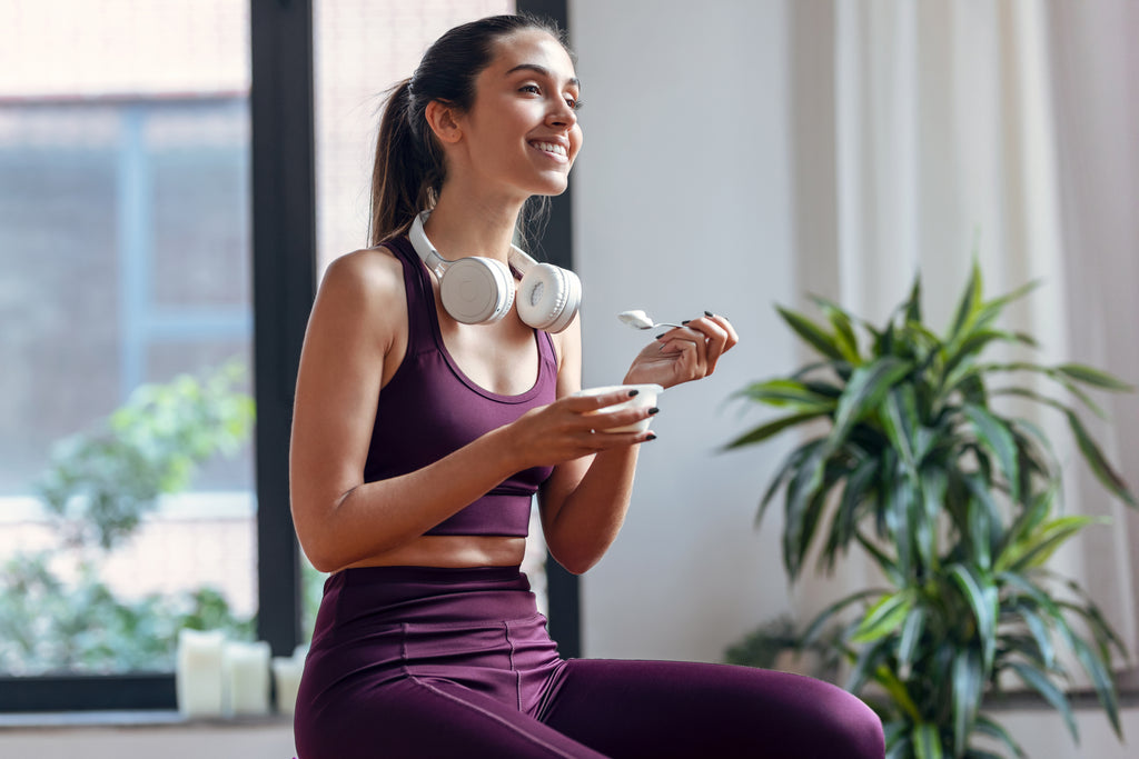 Shot of sporty young woman eating a yogurt while sitting on fitness ball at home.